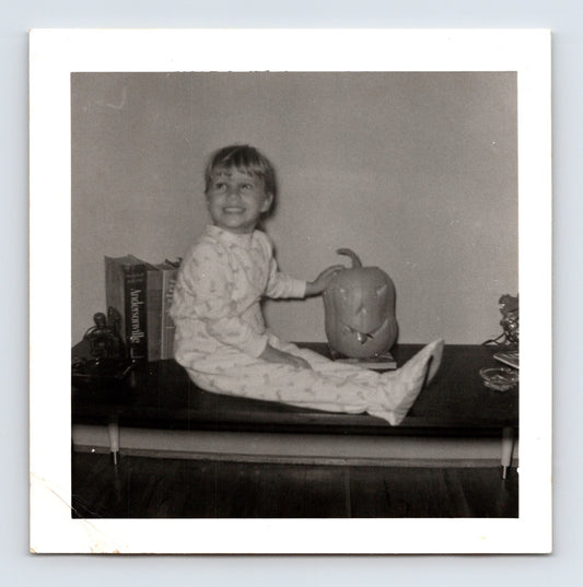 Vintage Halloween snapshot child sitting table jack o lantern pajamas 1950s square photo