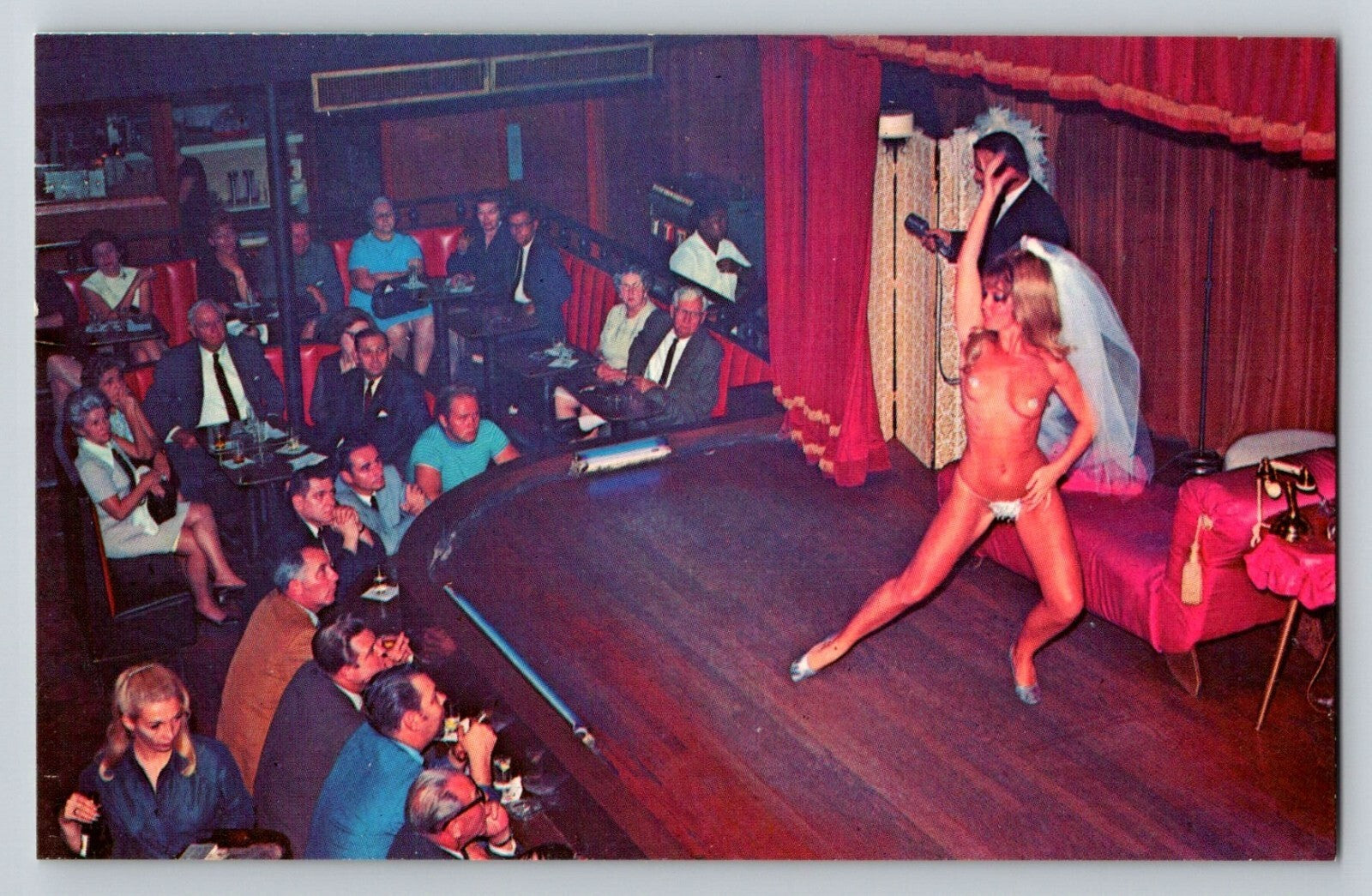 Burlesque dancer on stage in a theater with audience members watching.