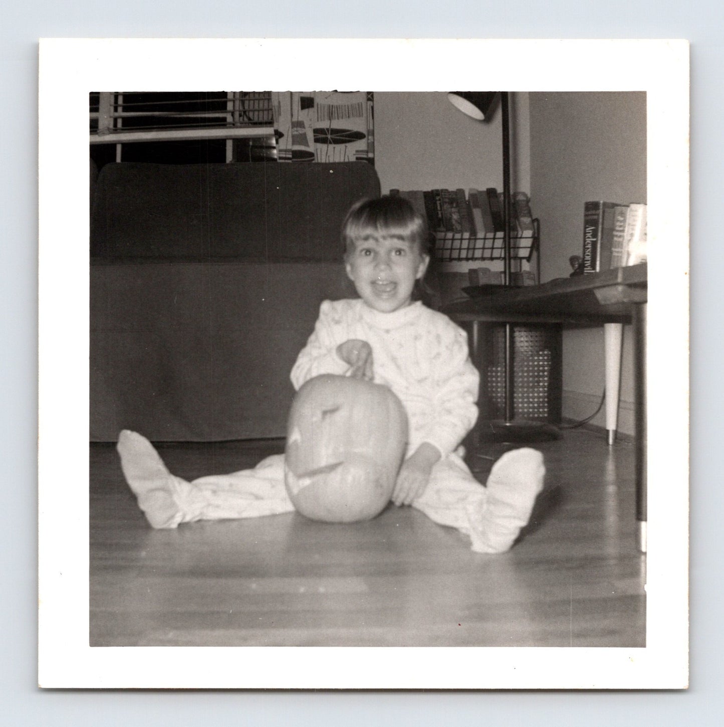 1940s Halloween snapshot photo child sitting with carved pumpkin jack o lantern indoors square format