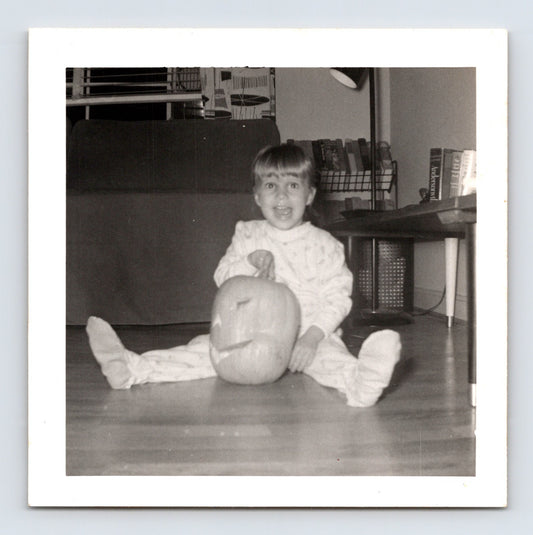 1940s Halloween snapshot photo child sitting with carved pumpkin jack o lantern indoors square format