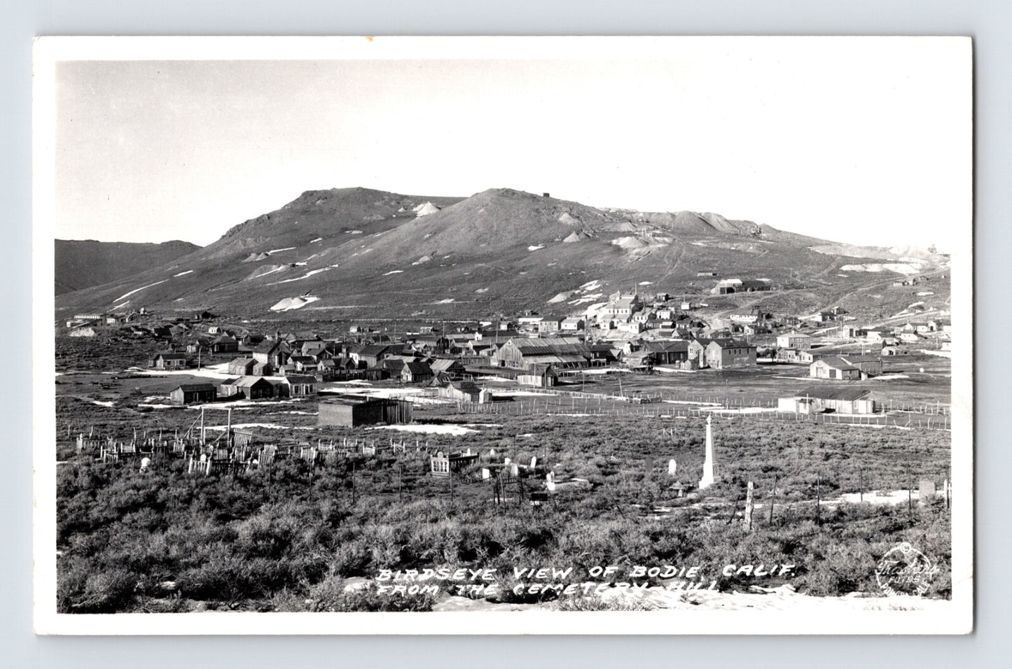 Black and white aerial view of Bodie California ghost town with cemetery in foreground and desert hills rising behind clustered wooden buildings