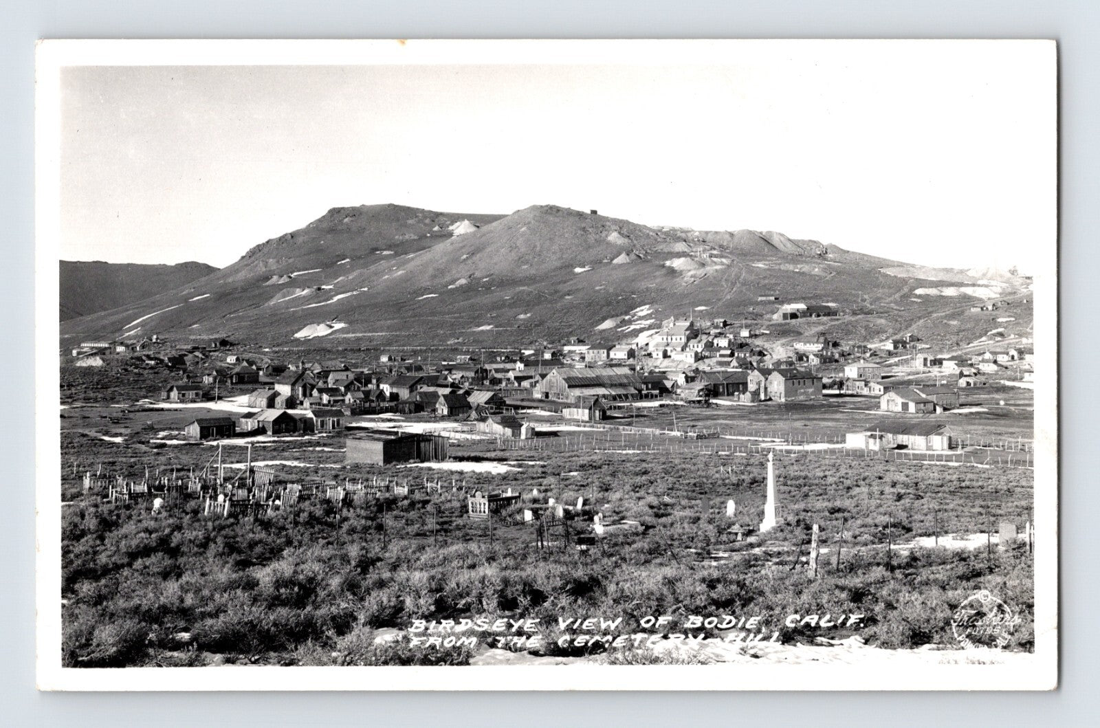 Black and white aerial view of Bodie California ghost town with cemetery in foreground and desert hills rising behind clustered wooden buildings