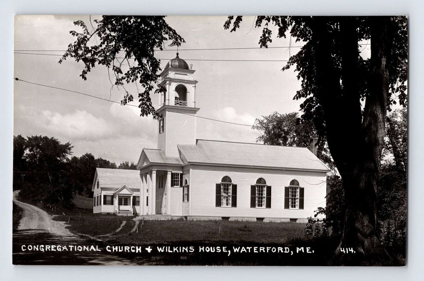 Black-and-white real photo postcard showing the Congregational Church and Wilkins House in Waterford, Maine, with a rural roadside setting and prominent church steeple.