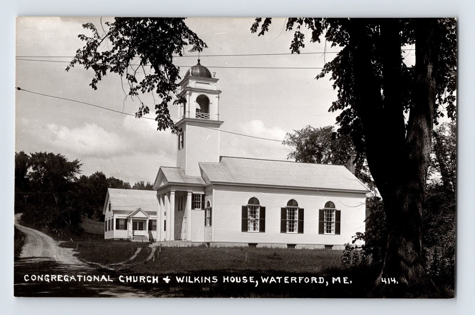 Black-and-white real photo postcard showing the Congregational Church and Wilkins House in Waterford, Maine, with a rural roadside setting and prominent church steeple.