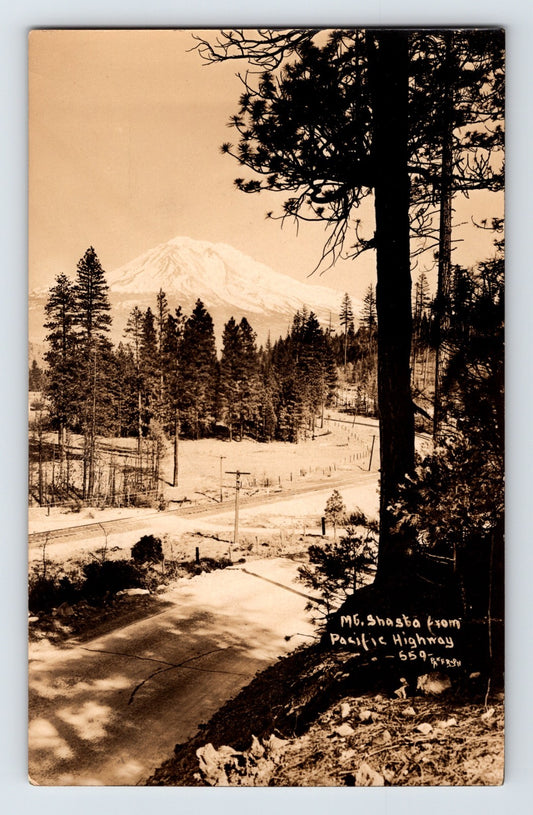 Mount Shasta California real photo postcard showing Pacific Highway roadway with forest foreground and snow-covered mountain peak.