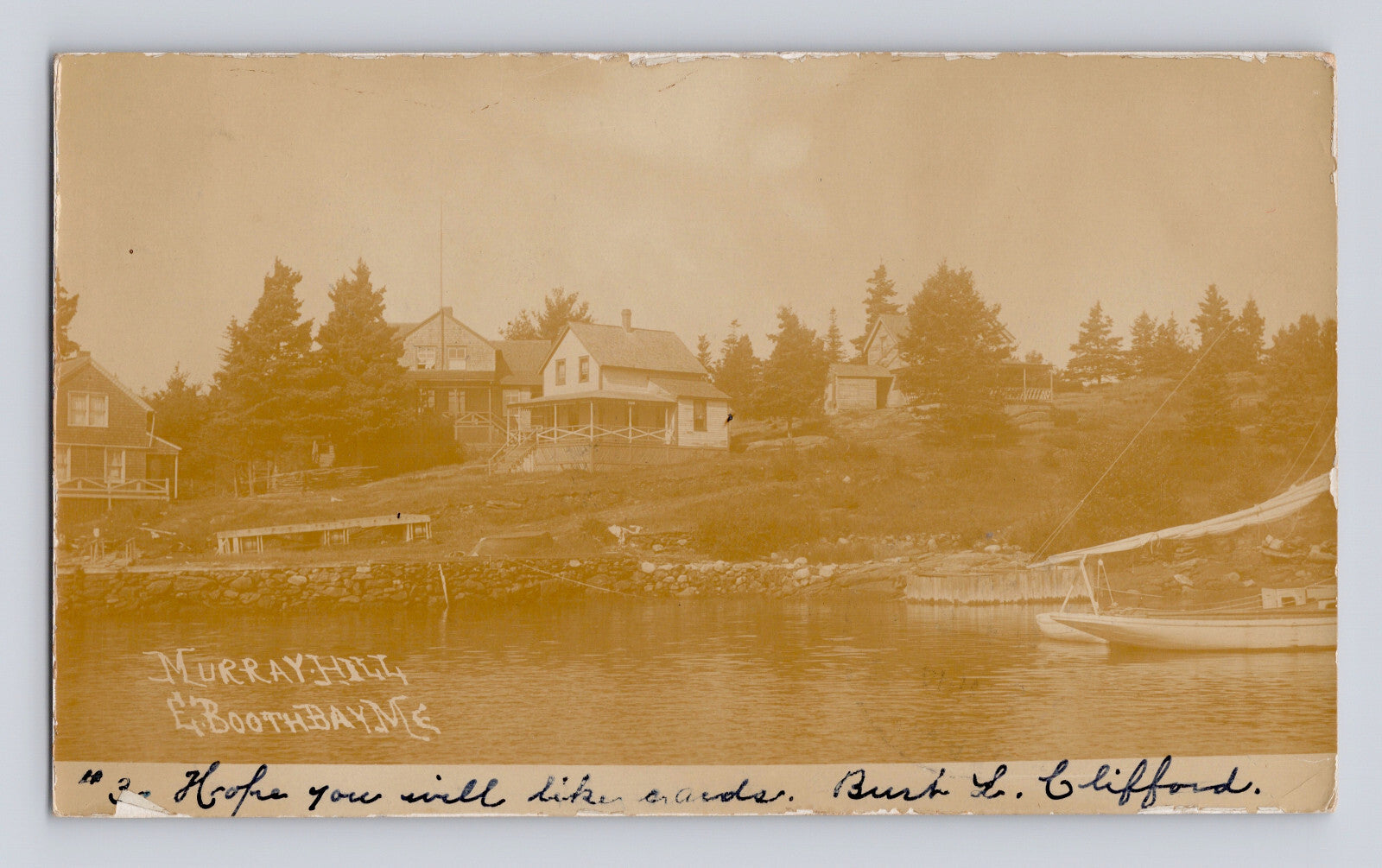Sepia-tone real photo postcard view of Murray Hill in Boothbay Harbor, Maine, showing waterfront homes, shoreline docks, and a small sailboat along the harbor.