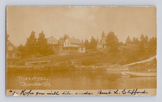 Sepia-tone real photo postcard view of Murray Hill in Boothbay Harbor, Maine, showing waterfront homes, shoreline docks, and a small sailboat along the harbor.