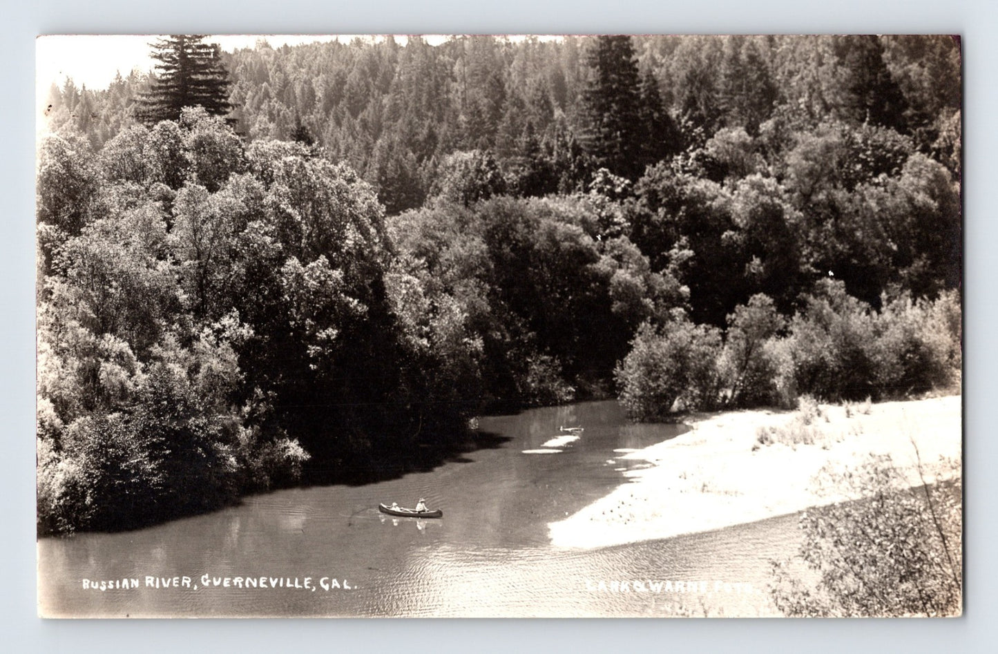 Russian River at Guerneville California with canoe on calm water beneath forested hills black and white real photo postcard