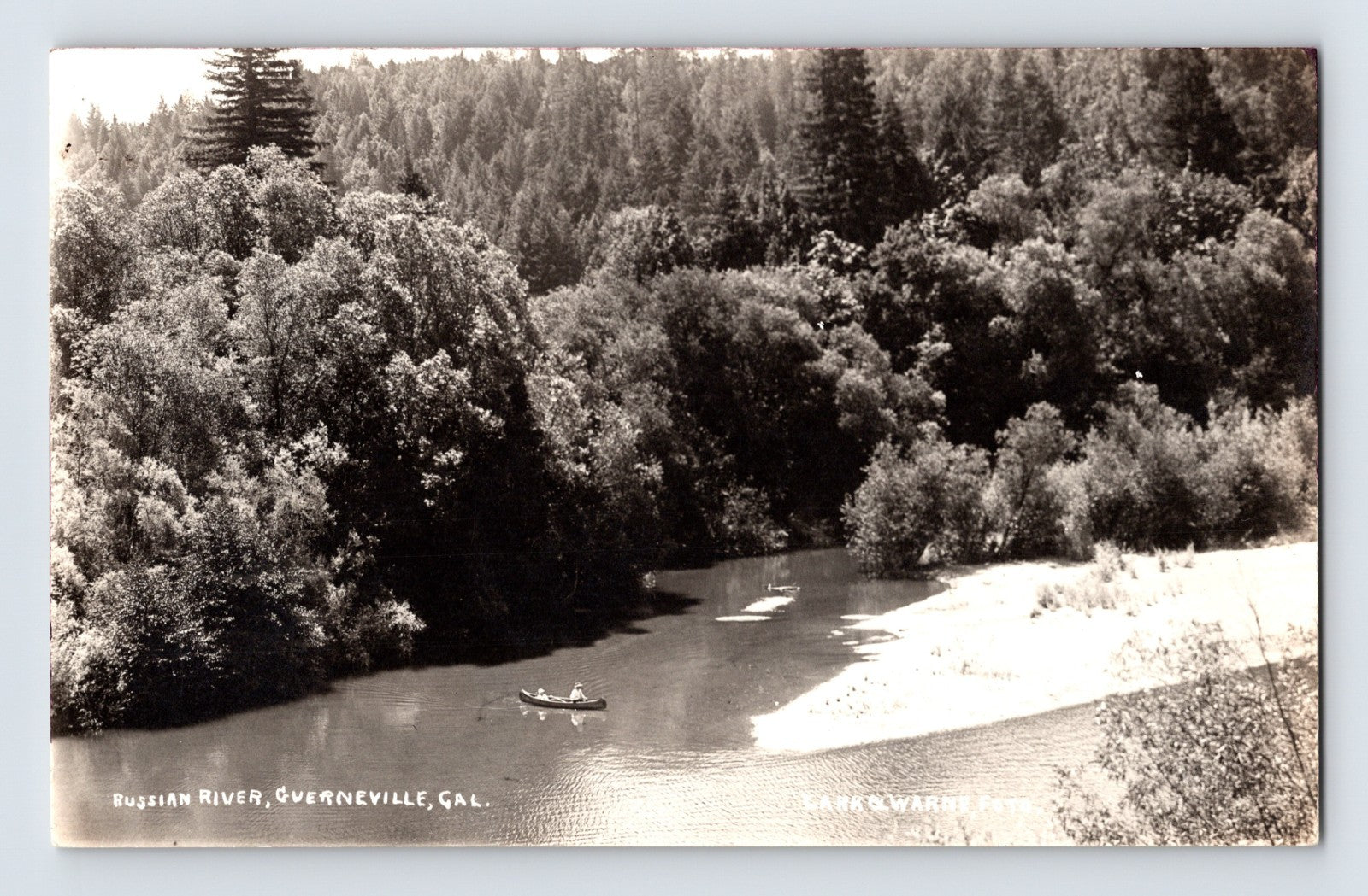 Russian River at Guerneville California with canoe on calm water beneath forested hills black and white real photo postcard
