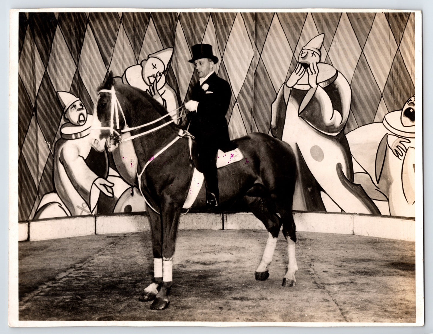 Circus dressage horse with rider in top hat performing before painted clown mural backdrop 1940s vintage photograph