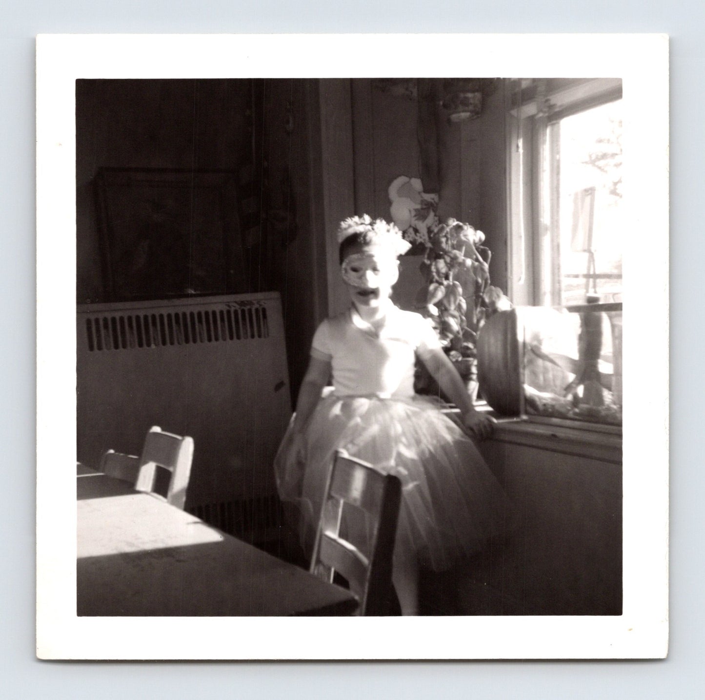 child in costume wearing mask and tulle skirt standing indoors by window Halloween snapshot photo