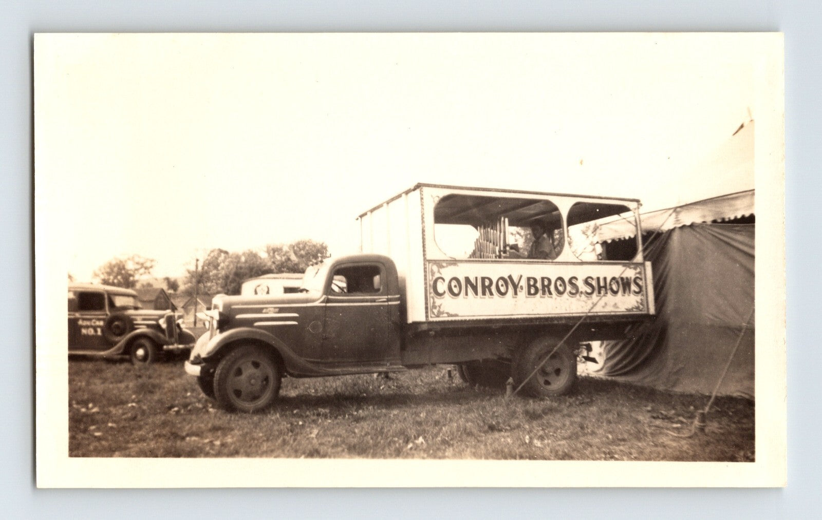 Conroy Bros Shows circus truck with open-sided calliope wagon body parked beside tent, 1940s photograph.