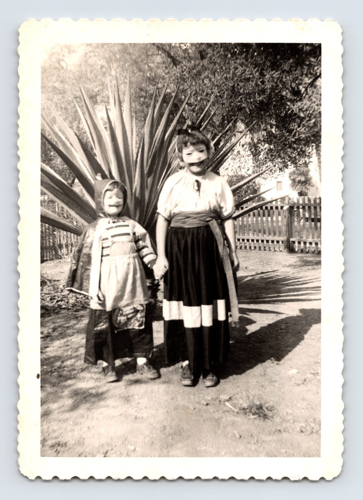 Two children Halloween costumes holding hands masks outdoor yard agave plant 1940s snapshot photo