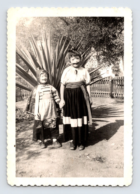 Two children Halloween costumes holding hands masks outdoor yard agave plant 1940s snapshot photo