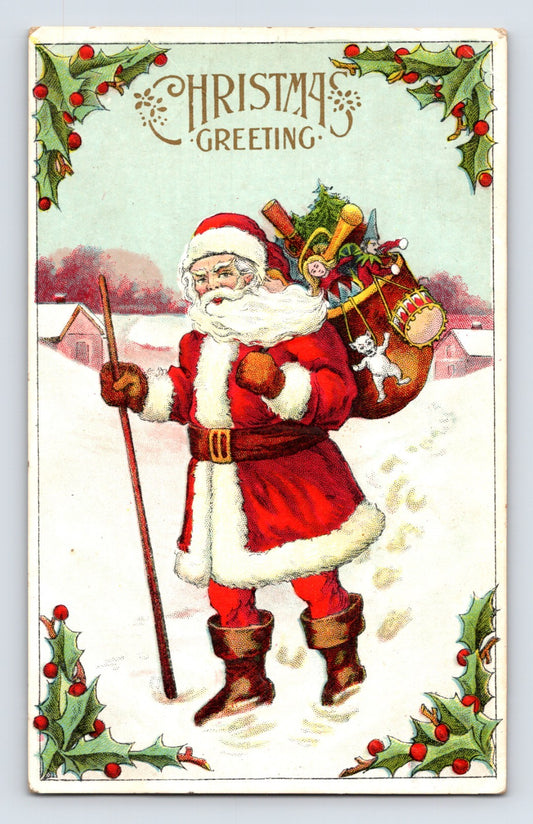 Santa Claus carrying sack of toys through snowy village framed by holly border on vintage Christmas greeting postcard.