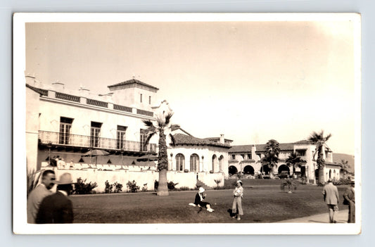 Sepia-toned real photo postcard showing the Hotel Playa complex in Ensenada, Baja California, with Spanish Colonial architecture, palm trees, and visitors on the grounds.
