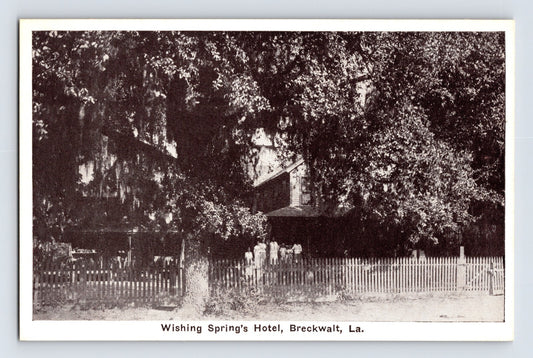 Black-and-white postcard view of Wishing Spring’s Hotel in Breckwalt, Louisiana, showing a shaded historic building behind a white picket fence beneath large oak trees.