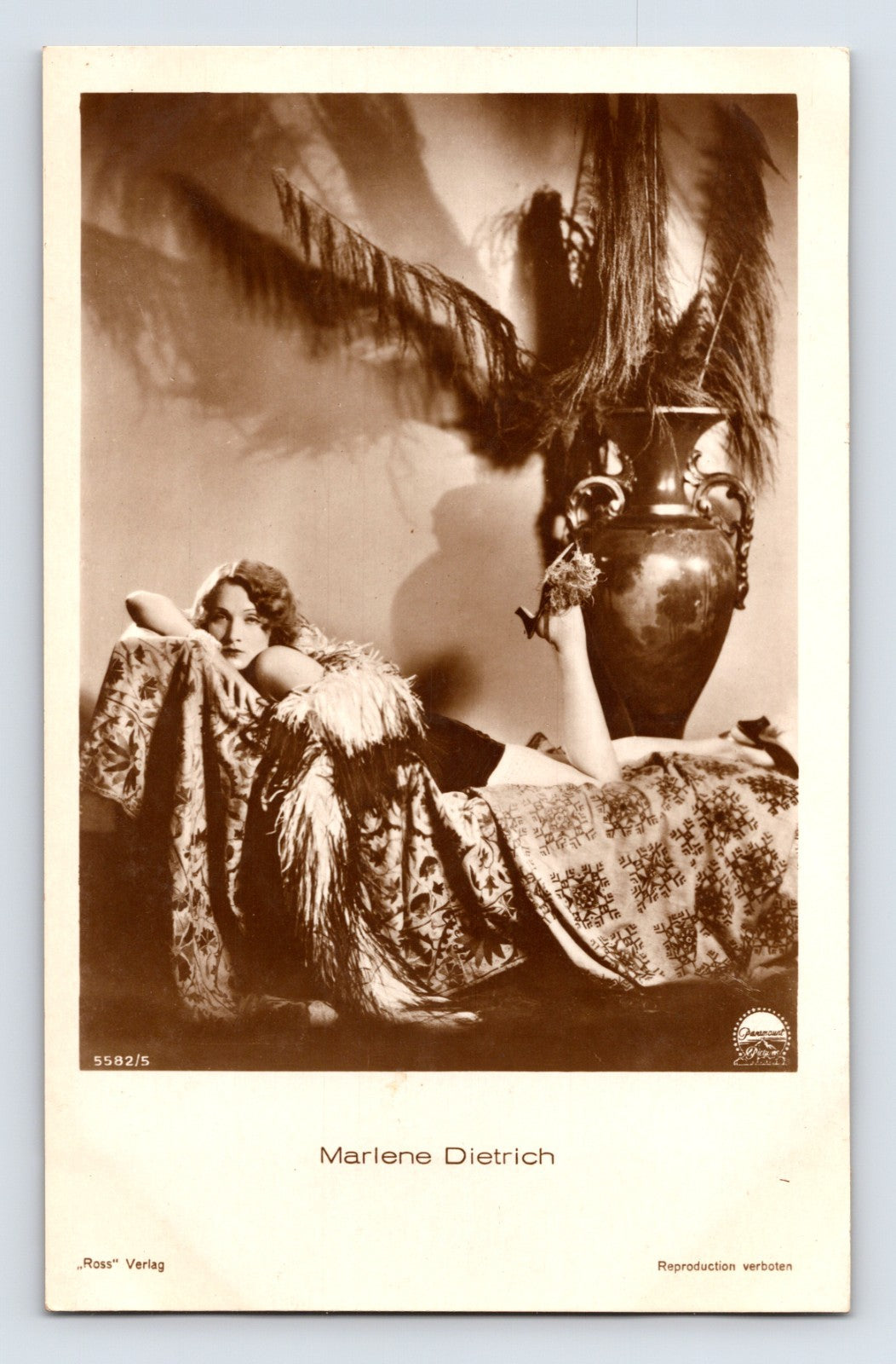 Real photo postcard of Marlene Dietrich reclining beside large decorative vase with feathers, 1930s Ross Verlag studio portrait