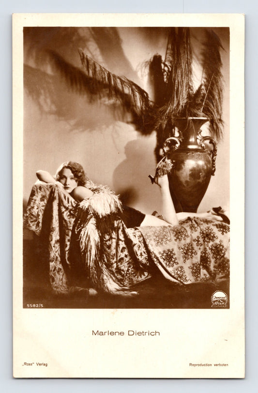 Real photo postcard of Marlene Dietrich reclining beside large decorative vase with feathers, 1930s Ross Verlag studio portrait