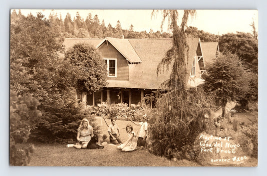 1940s real photo postcard of Casa Del Noyo in Fort Bragg, California with children seated on lawn in front of large wooden house surrounded by trees