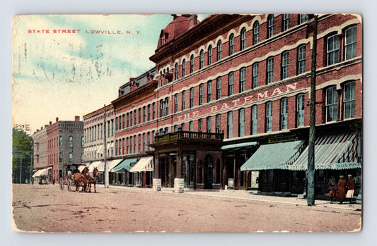 1914 postcard view of State Street in Lowville, New York, featuring the Bateman Hotel, storefront awnings, pedestrians, and horse-drawn wagons along the commercial district.