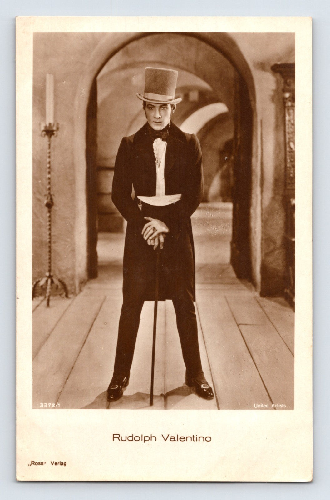 1930s postcard portrait of silent film star Rudolph Valentino standing in formal attire with top hat and cane in a dramatic studio scene published by Ross Verlag.