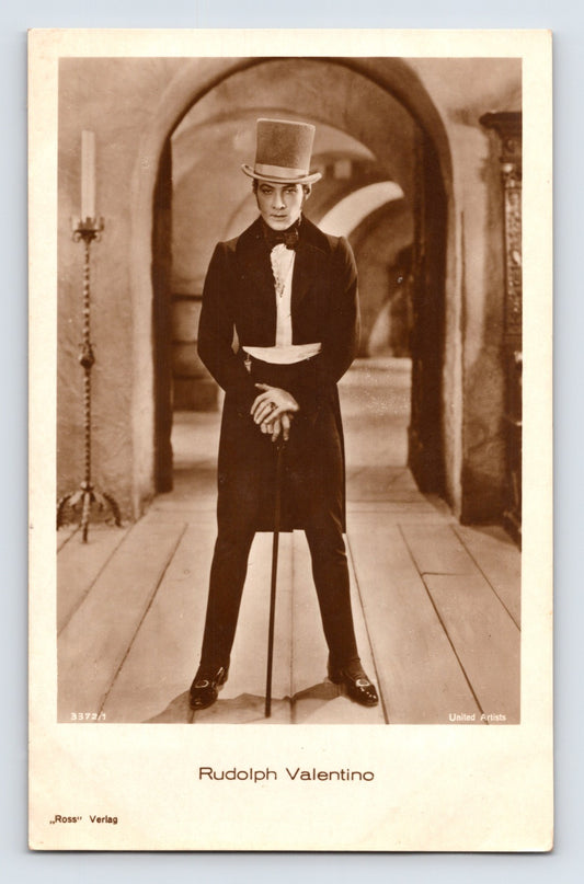 1930s postcard portrait of silent film star Rudolph Valentino standing in formal attire with top hat and cane in a dramatic studio scene published by Ross Verlag.