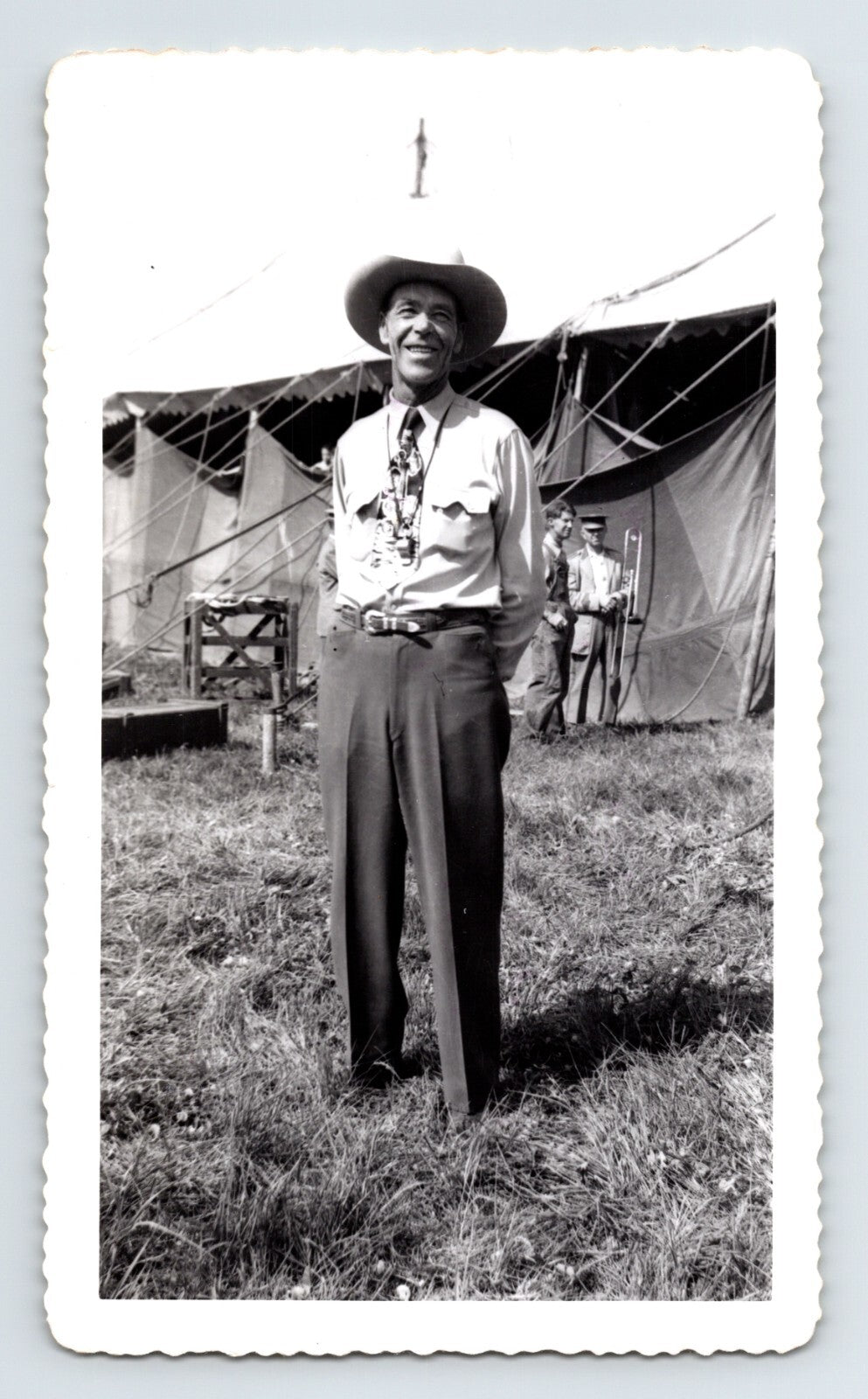 Black and white photo of a man standing outdoors with tents in the background