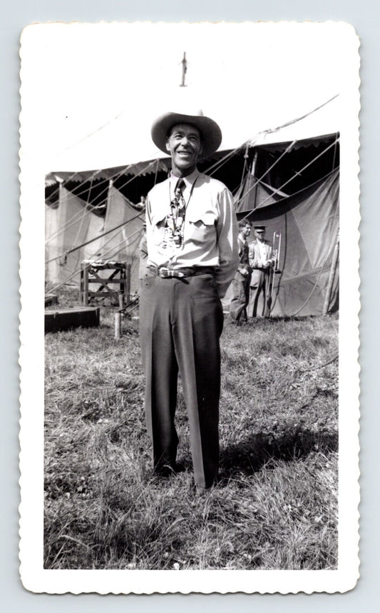 Black and white photo of a man standing outdoors with tents in the background