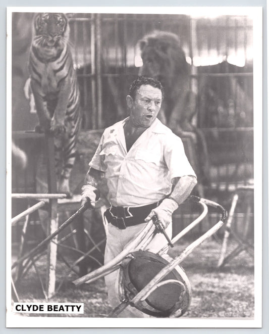1940s press photograph of Clyde Beatty inside circus animal cage holding chair and whip, with tiger and lion visible behind him.