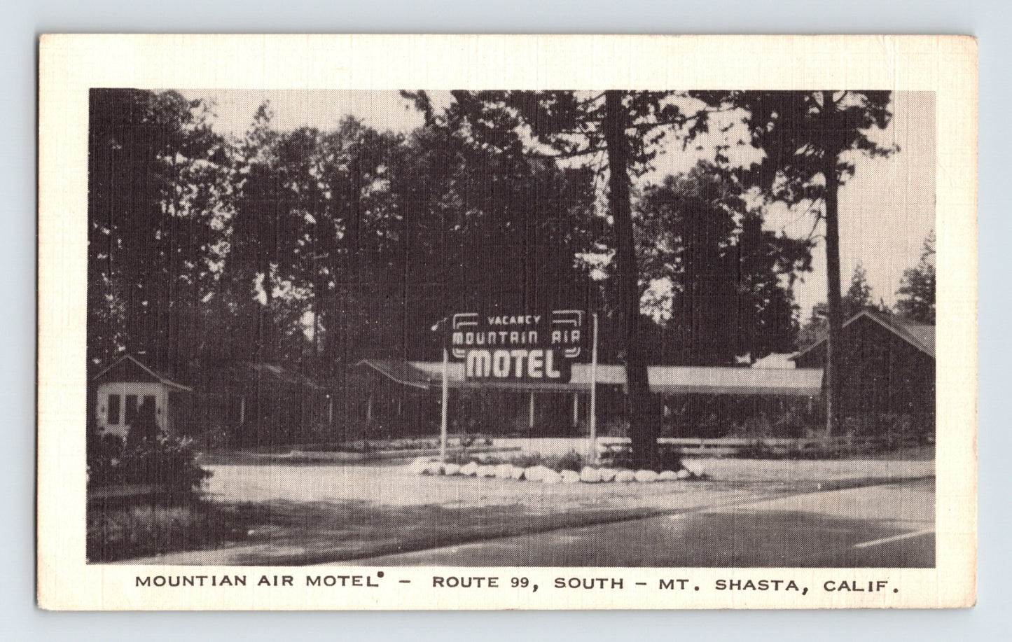 Black and white postcard of Mountain Air Motel on Route 99 in Mt Shasta California with roadside sign and pine trees