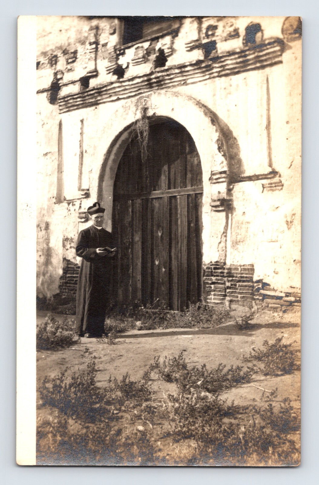 Vintage photograph of a person standing in front of a large wooden door on a stone building.