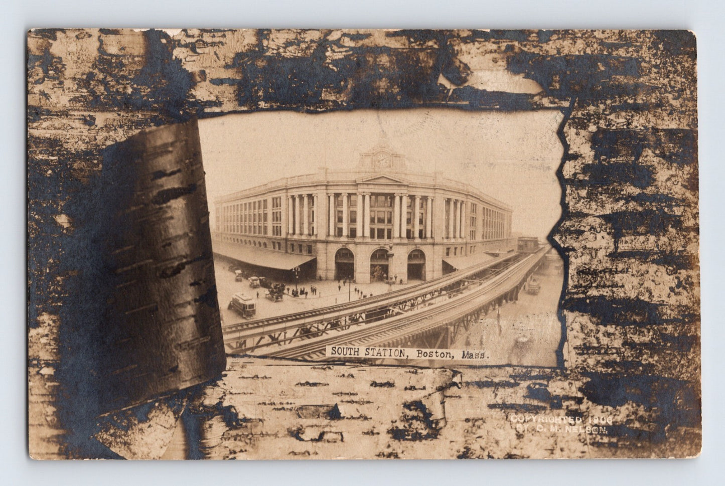 1907 real photo postcard showing South Station in Boston, Massachusetts, framed within a decorative birch bark novelty design with elevated rail approaches and station crowds visible below.