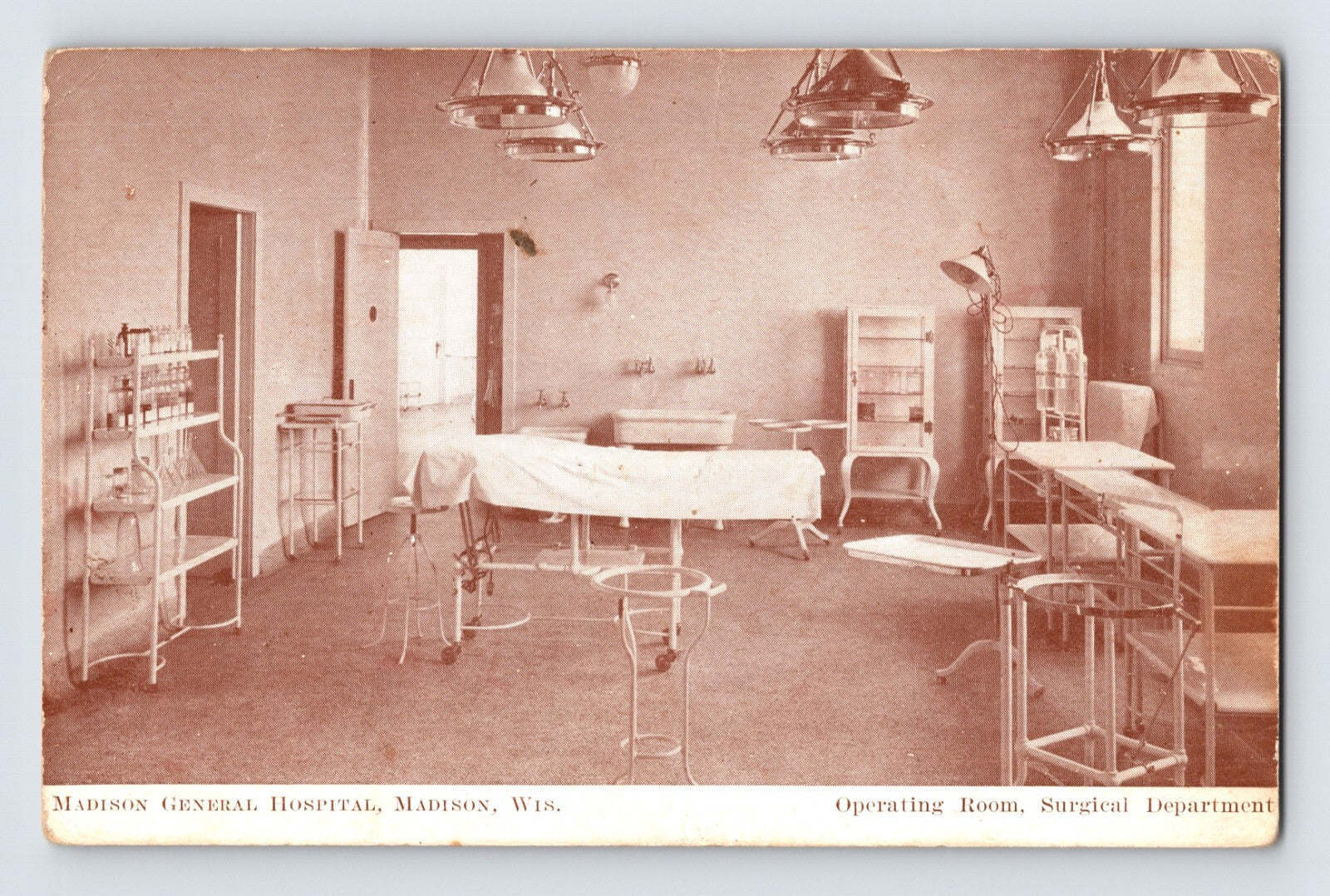 1910s postcard of Madison General Hospital operating room in Madison, Wisconsin with central surgical table, overhead lamps, metal instrument stands, and glass cabinets