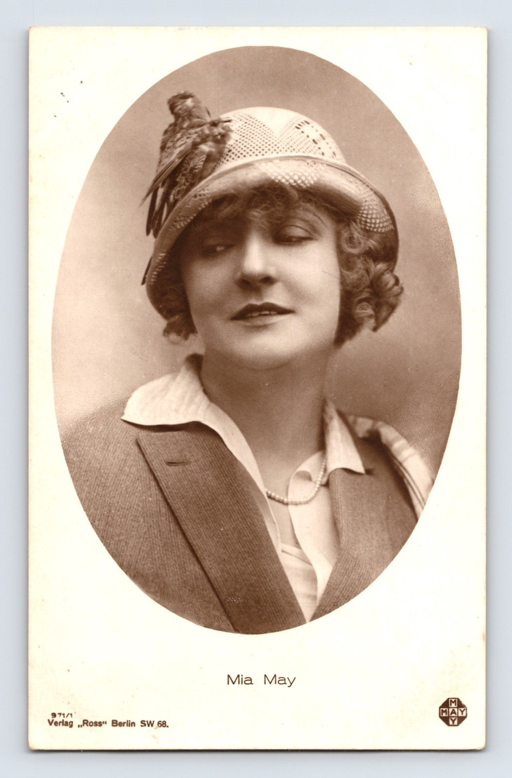 Sepia-tone German actress postcard portrait of silent film star Mia May wearing a cloche-style hat with feather detail and tailored jacket, published in Berlin.