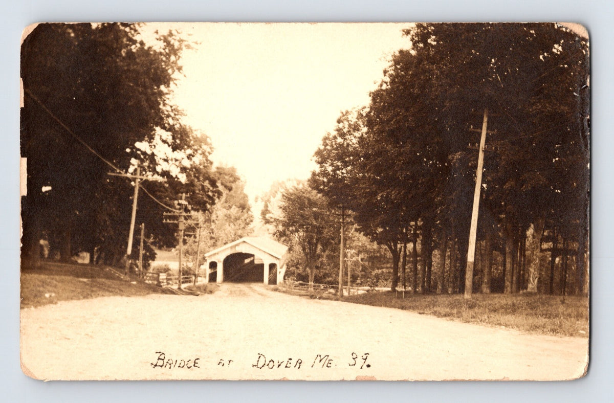 Postcard front showing a covered wooden bridge along a rural road lined with trees and telegraph poles at Dover, Maine; divided back with AZO stamp box, unposted, 1910s.