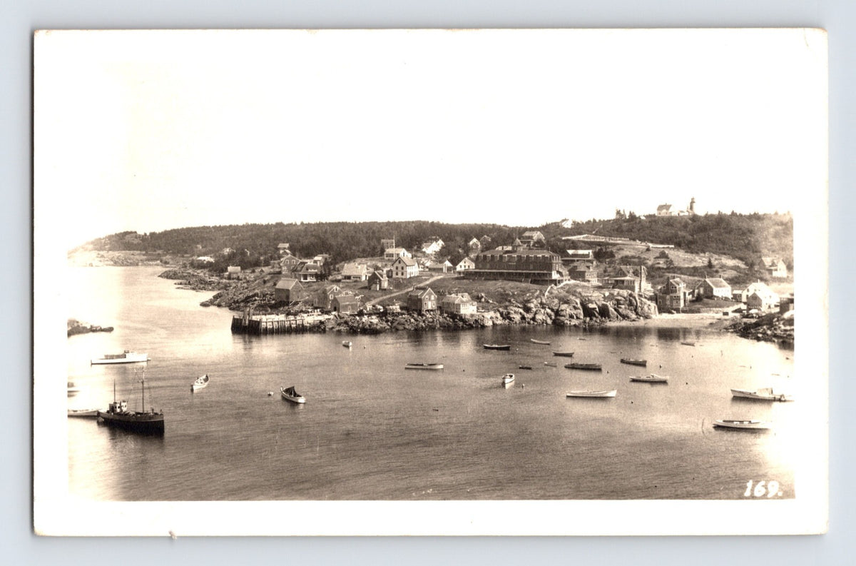Monhegan Maine village harbor with boats, pier and clustered shoreline buildings in elevated 1956 real photo view