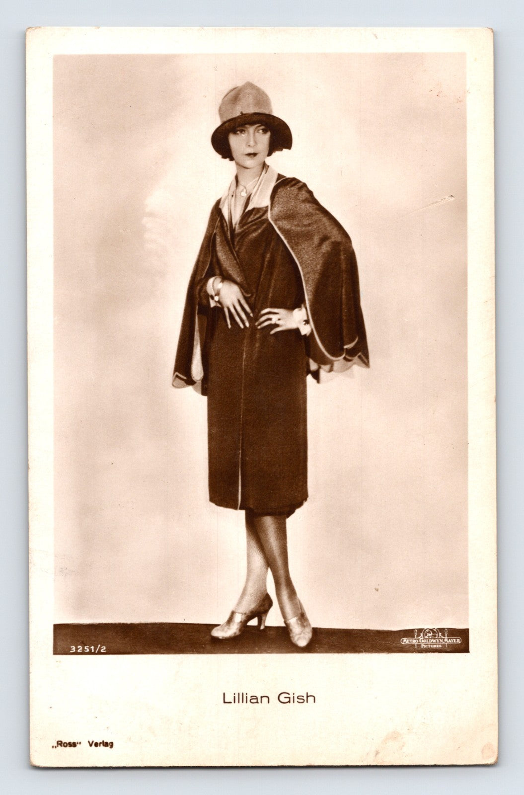 Sepia-tone full-length portrait postcard of silent film actress Lillian Gish wearing a cloche hat and fashionable dark dress in a studio publicity photograph.