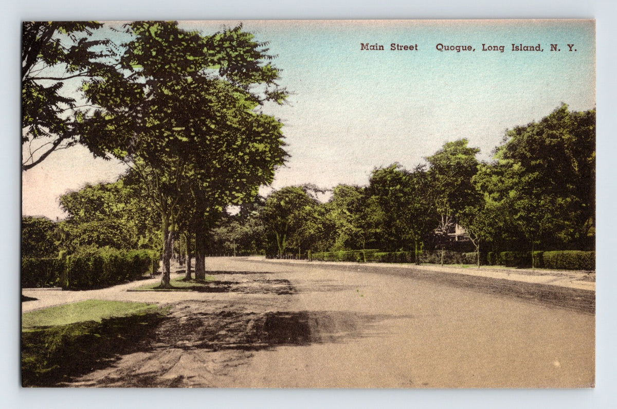 Hand-colored postcard view of Main Street in Quogue Long Island New York showing a tree-lined road with sidewalks and residential hedges