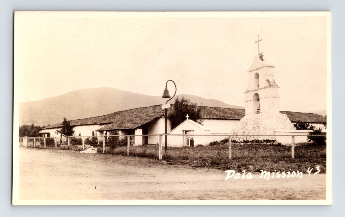Pala California Mission Camino Real RPPC postcard with bell tower adobe buildings and rural roadside setting