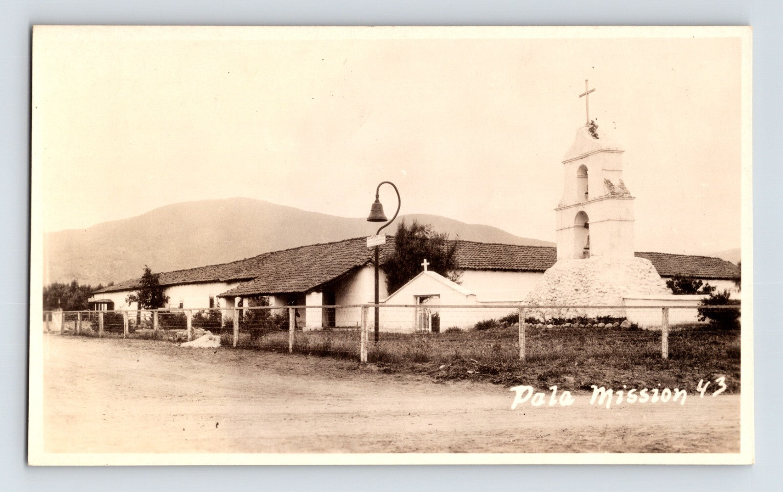Pala California Mission Camino Real RPPC postcard with bell tower adobe buildings and rural roadside setting