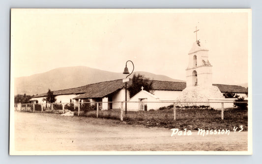 Pala California Mission Camino Real RPPC postcard with bell tower adobe buildings and rural roadside setting