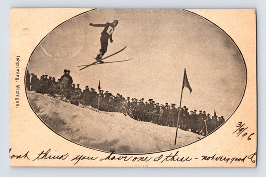Ishpeming Michigan ski jumping postcard showing an early skier airborne above a crowd during a winter sporting exhibition.