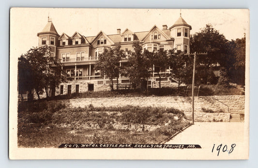 Sepia real photo postcard of Hotel Castle Rock overlooking hillside in Excelsior Springs Missouri with multi gabled rooflines and wraparound porch 1909