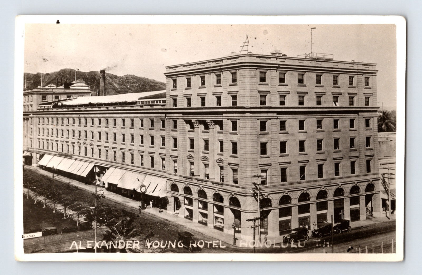 Real photo postcard of Alexander Young Hotel in Honolulu Hawaii showing multi story corner building with arched ground floor and early automobiles
