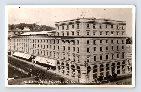 Real photo postcard of Alexander Young Hotel in Honolulu Hawaii showing multi story corner building with arched ground floor and early automobiles