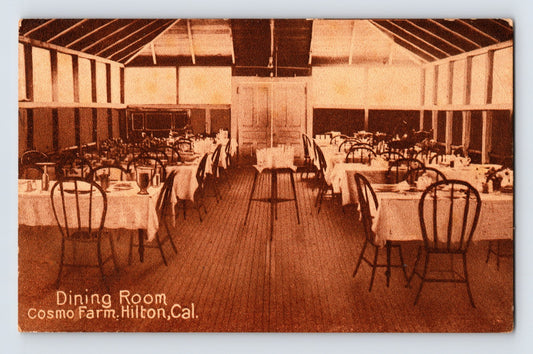 Hilton California Cosmo Farm dining room postcard showing long rustic dining hall interior with white tablecloth tables and wooden chairs arranged beneath exposed rafters.