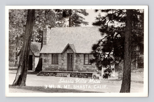 1940s real photo postcard showing the Shasta Villa Motel near Mount Shasta, California, featuring a rustic stone cottage surrounded by tall pine trees.