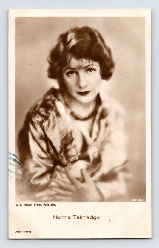 Sepia-tone portrait postcard of silent film actress Norma Talmadge wearing a satin wrap and necklace in a softly lit studio photograph.