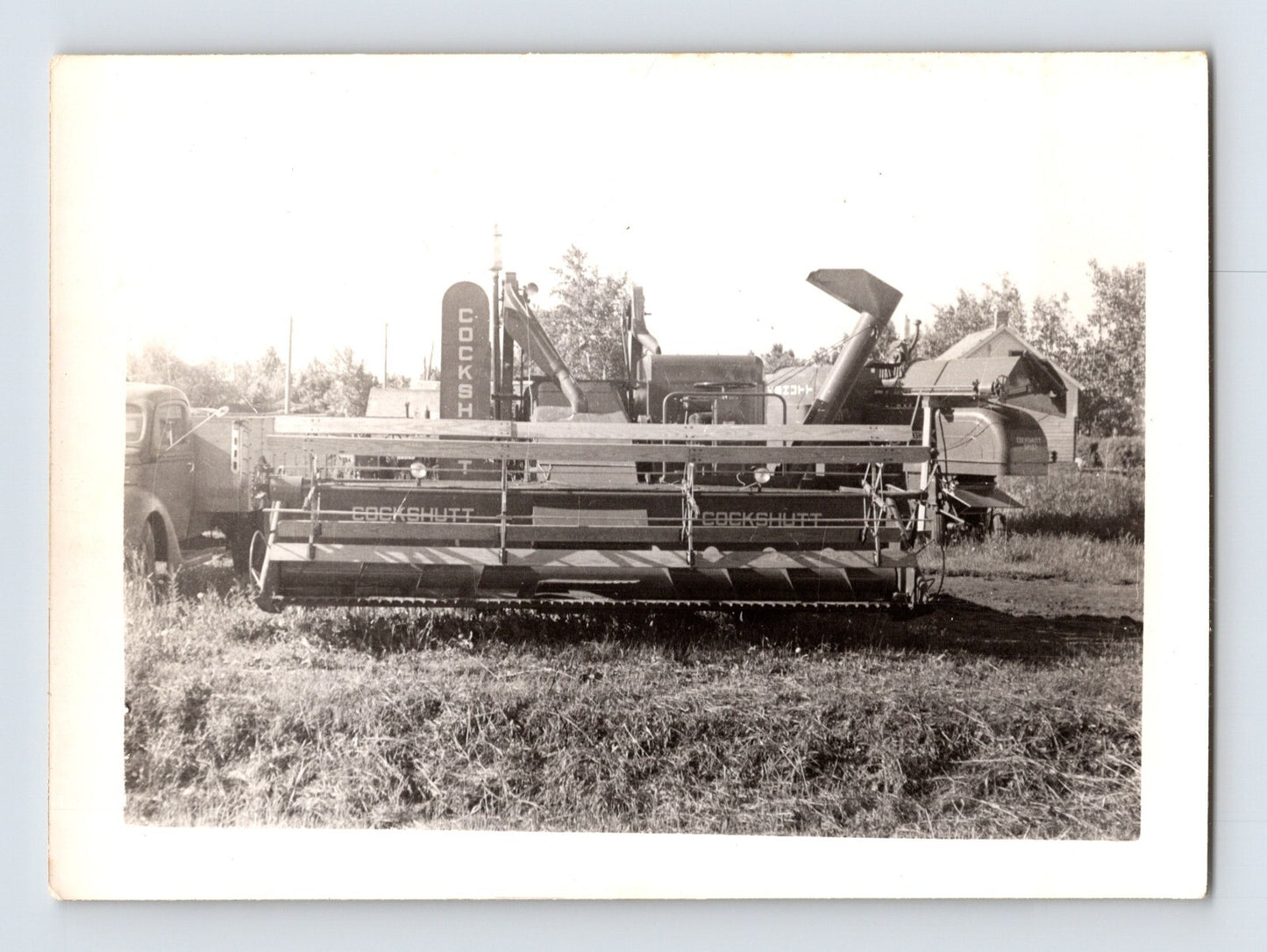 Vintage black and white photograph of a combine harvester in a field.